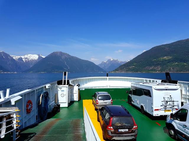 Cars parked on a ferry deck crossing a scenic Norwegian fjord during a road trip